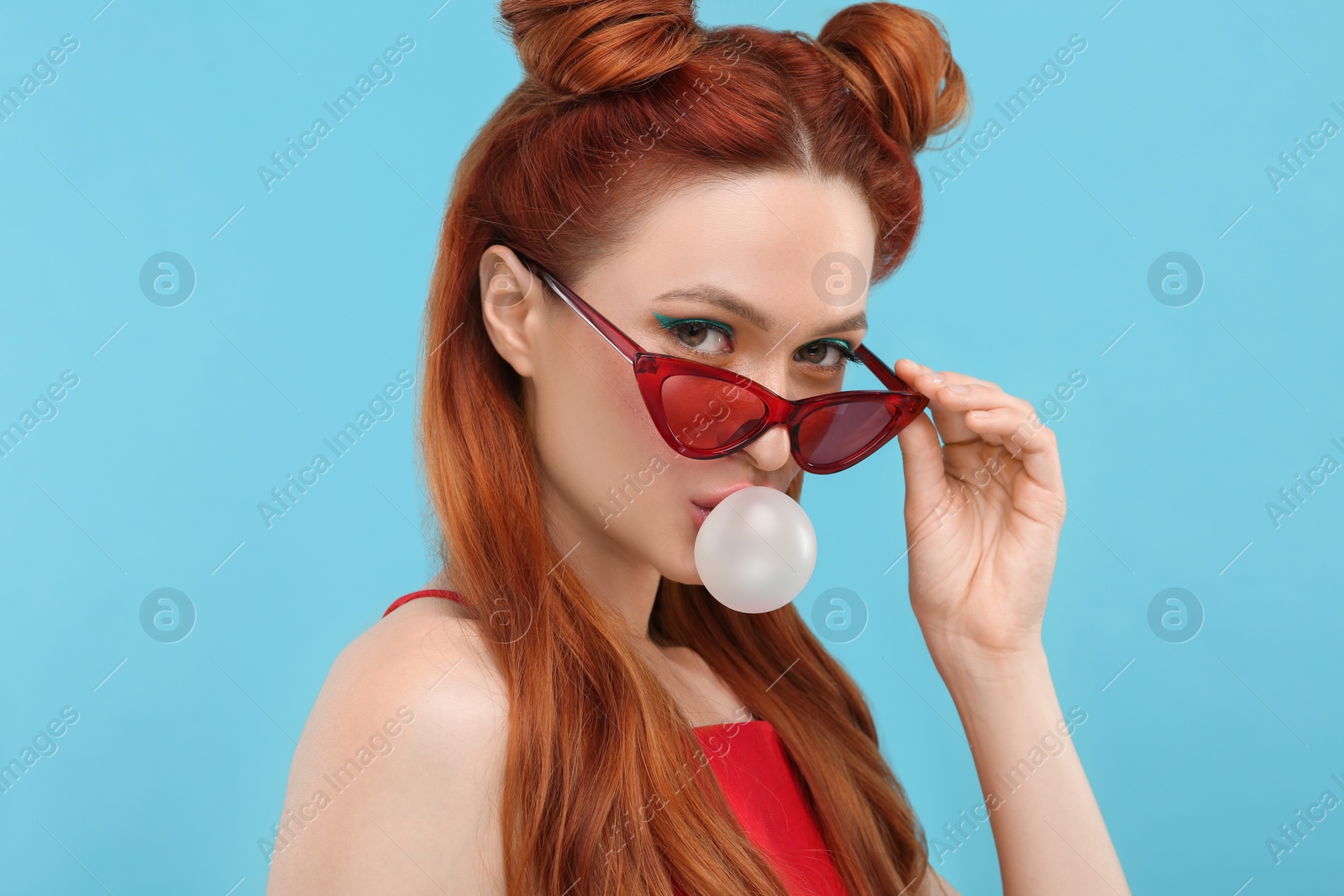 Photo of Portrait of beautiful woman in sunglasses blowing bubble gum on light blue background