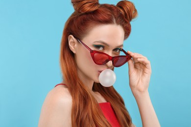 Photo of Portrait of beautiful woman in sunglasses blowing bubble gum on light blue background