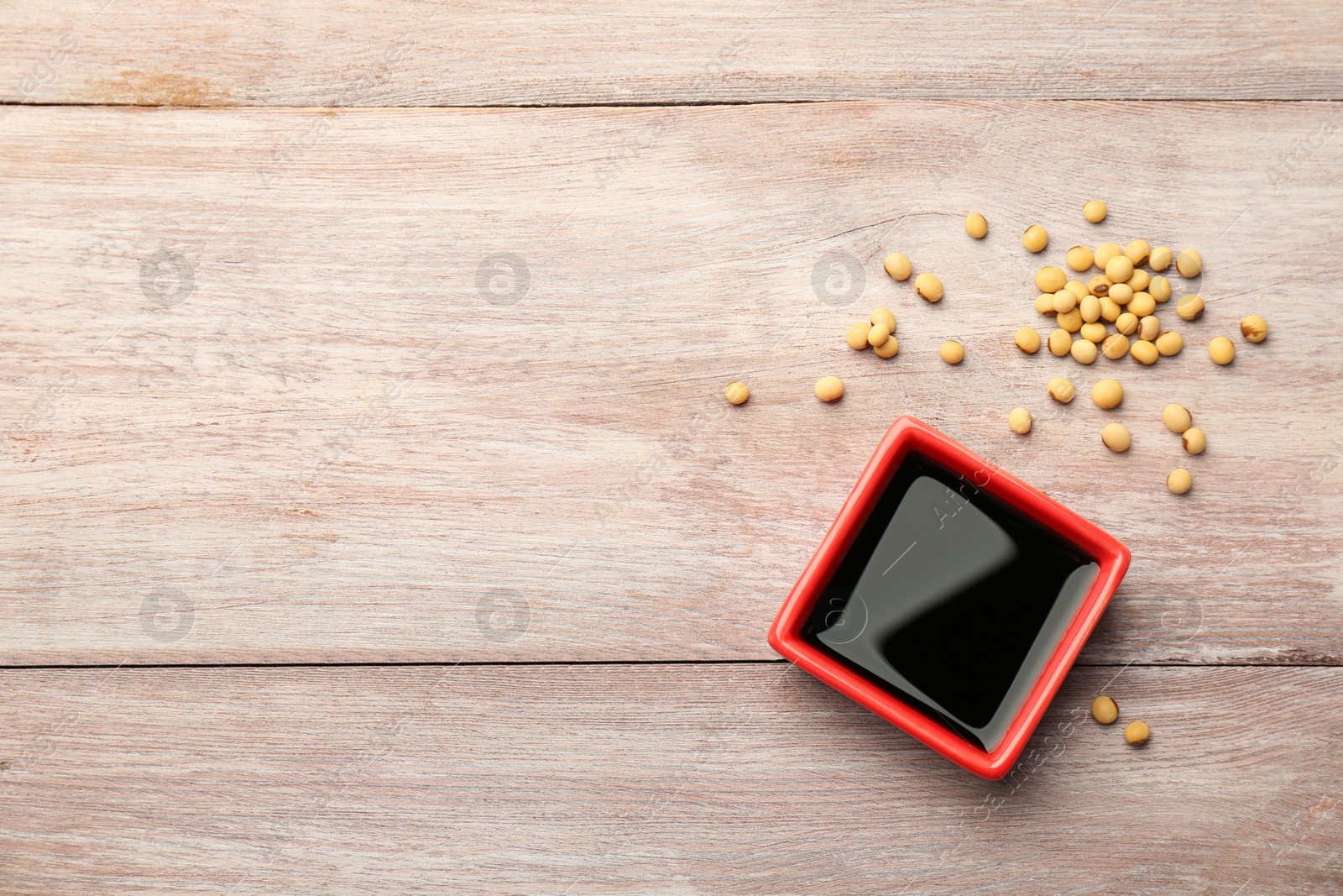 Photo of Soy sauce in bowl, soybeans and chopsticks on wooden table, flat lay. Space for text