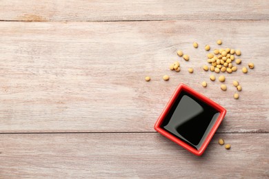 Soy sauce in bowl, soybeans and chopsticks on wooden table, flat lay. Space for text