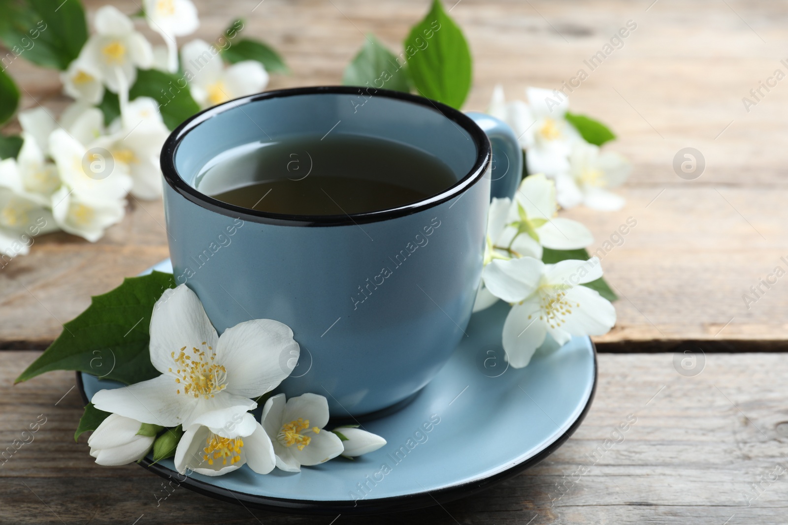 Photo of Cup of tea and fresh jasmine flowers on wooden table