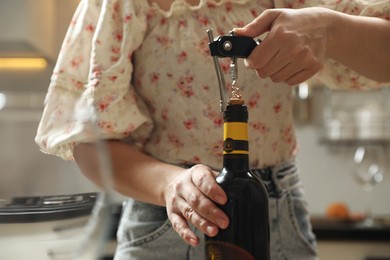 Woman opening wine bottle with corkscrew on blurred background, closeup