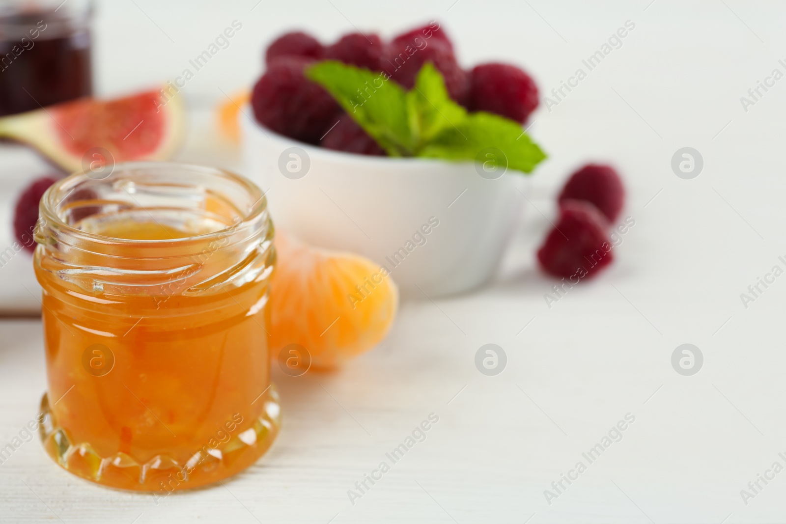 Photo of Open glass jar of sweet jam on white wooden table, closeup. Space for text