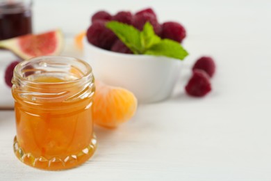 Photo of Open glass jar of sweet jam on white wooden table, closeup. Space for text