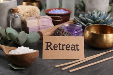 Photo of Card with word Retreat and different spa products on dark grey table