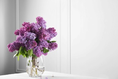 Beautiful lilac flowers in vase on white table near wall, space for text