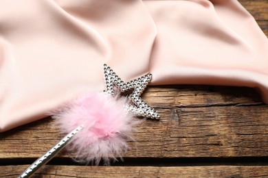 Photo of Beautiful silver magic wand with feather and pink fabric on wooden table, closeup