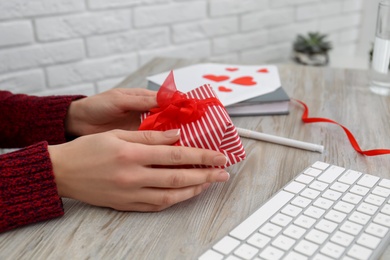 Woman with gift box at workplace, closeup. Valentine's Day celebration