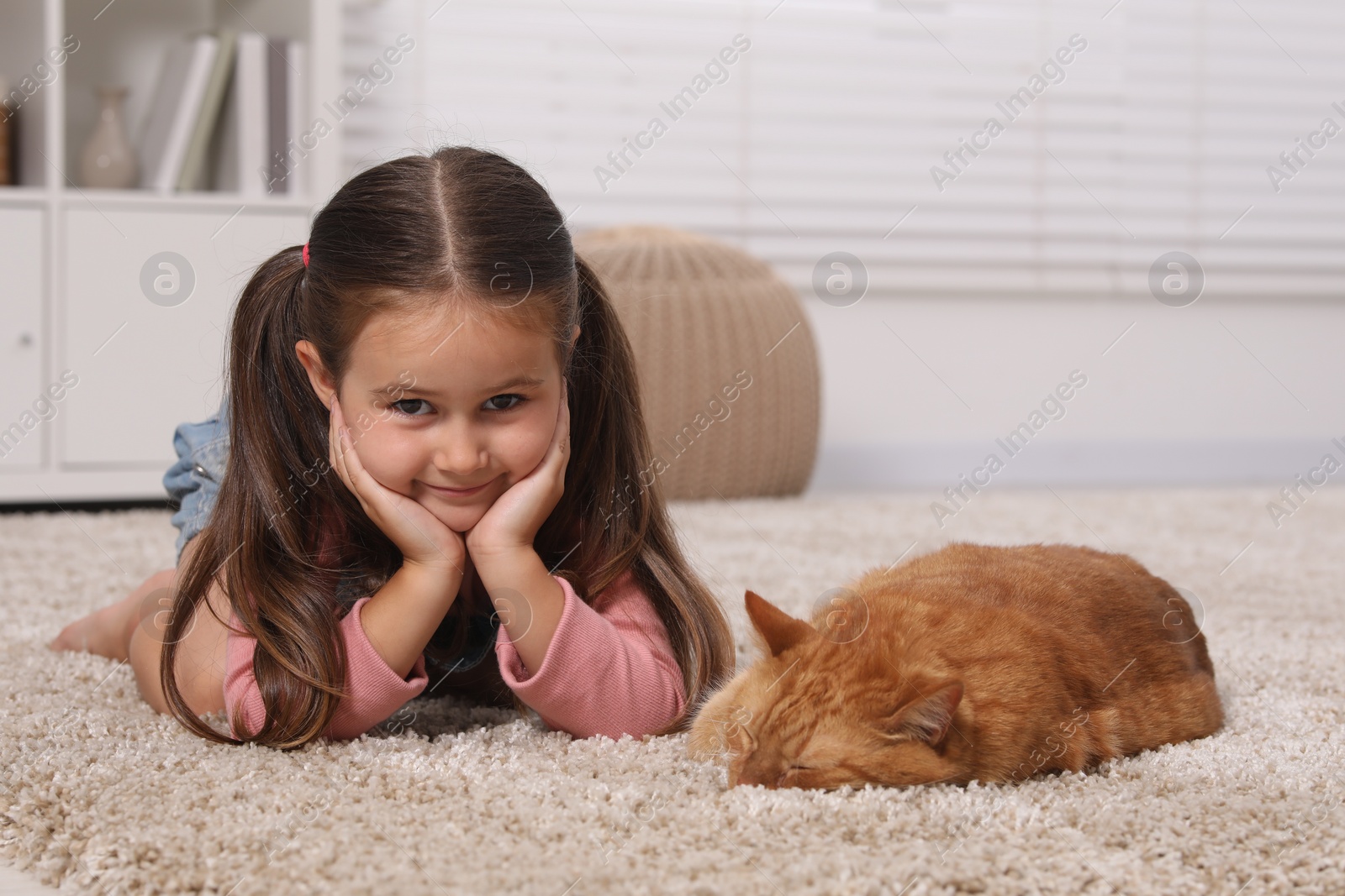 Photo of Smiling little girl and cute ginger cat on carpet at home