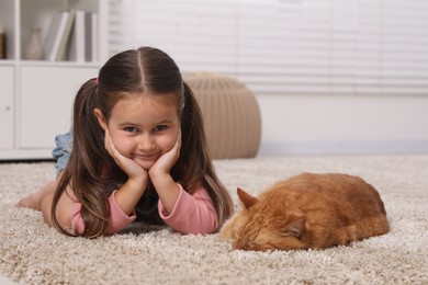 Smiling little girl and cute ginger cat on carpet at home