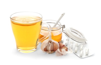 Photo of Cup with hot tea, honey, garlic and pills as cold remedies on white background