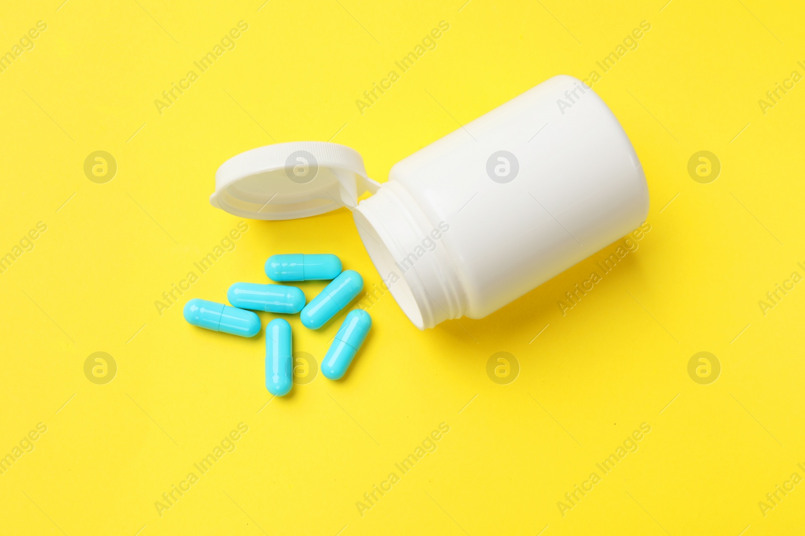 Photo of Vitamin capsules and bottle on yellow background, top view