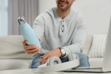 Man holding thermo bottle at home, closeup