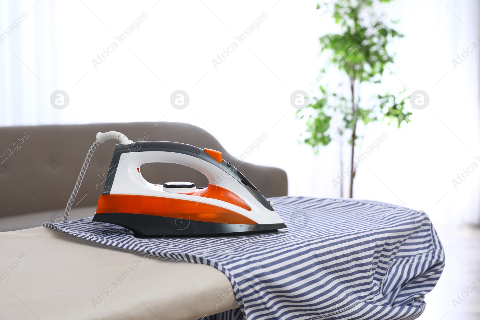 Photo of Modern electric iron and shirt on board indoors. Space for text