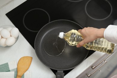 Photo of Woman pouring cooking oil from bottle into frying pan in kitchen, top view