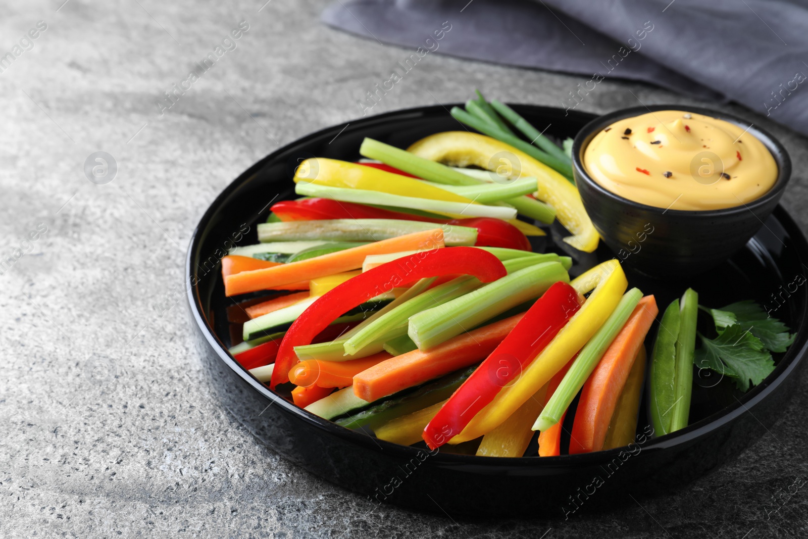 Photo of Fresh raw vegetable sticks and sauce on grey table