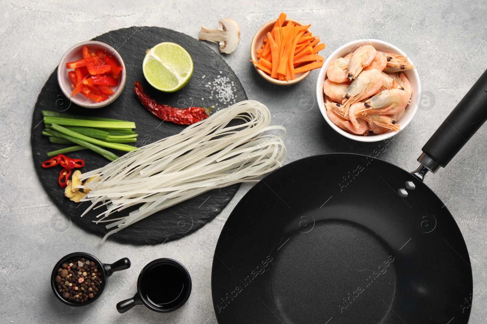 Photo of Flat lay composition with black wok, spices and products on grey textured table