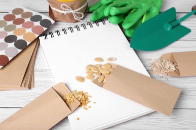 Photo of Many different vegetable seeds and notebook on white wooden table