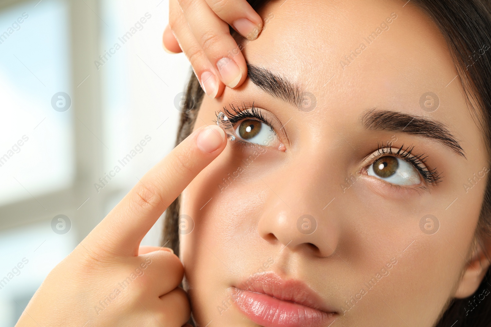 Photo of Woman putting contact lens in her eye indoors, closeup view