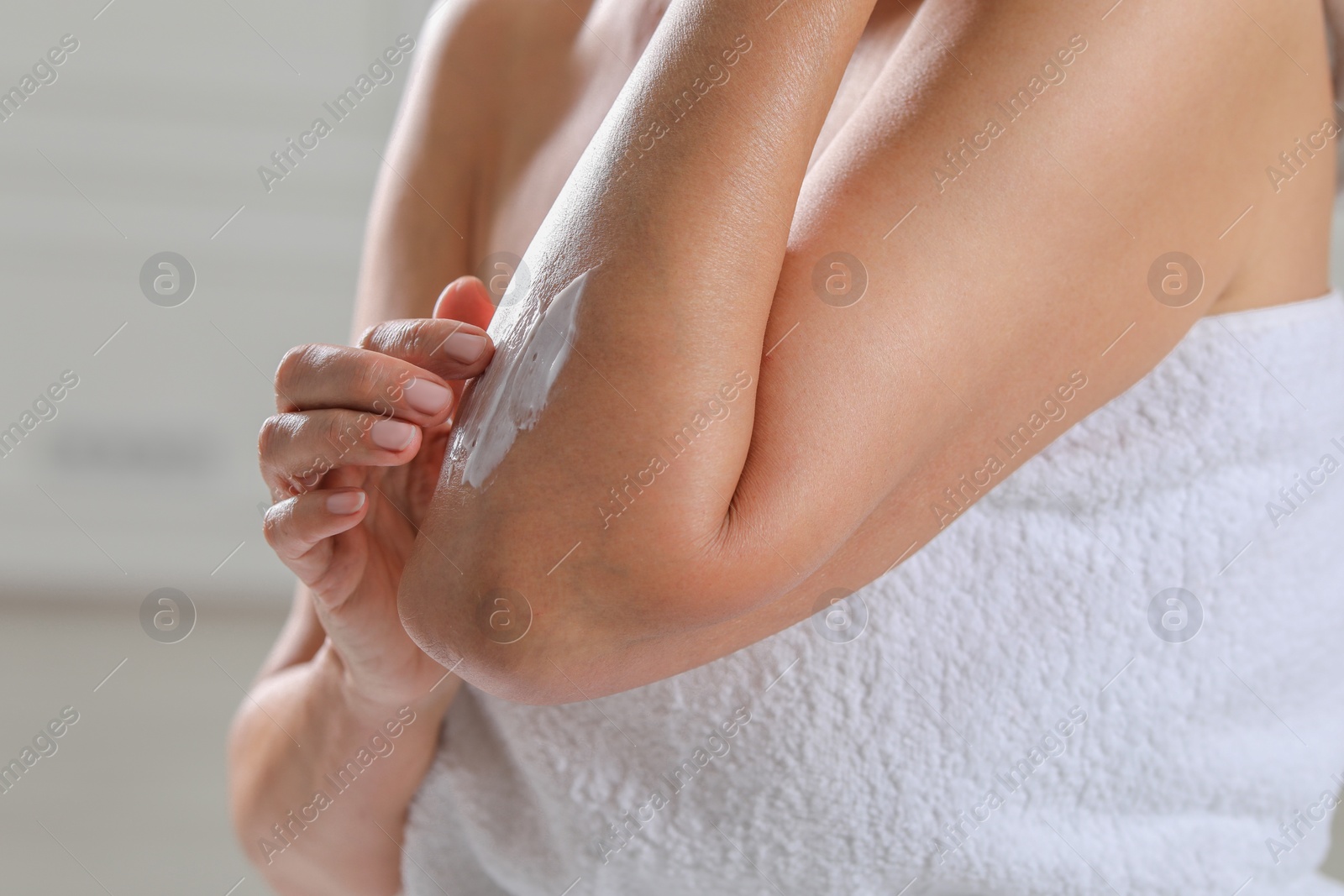 Photo of Woman applying body cream onto arm on blurred background, closeup