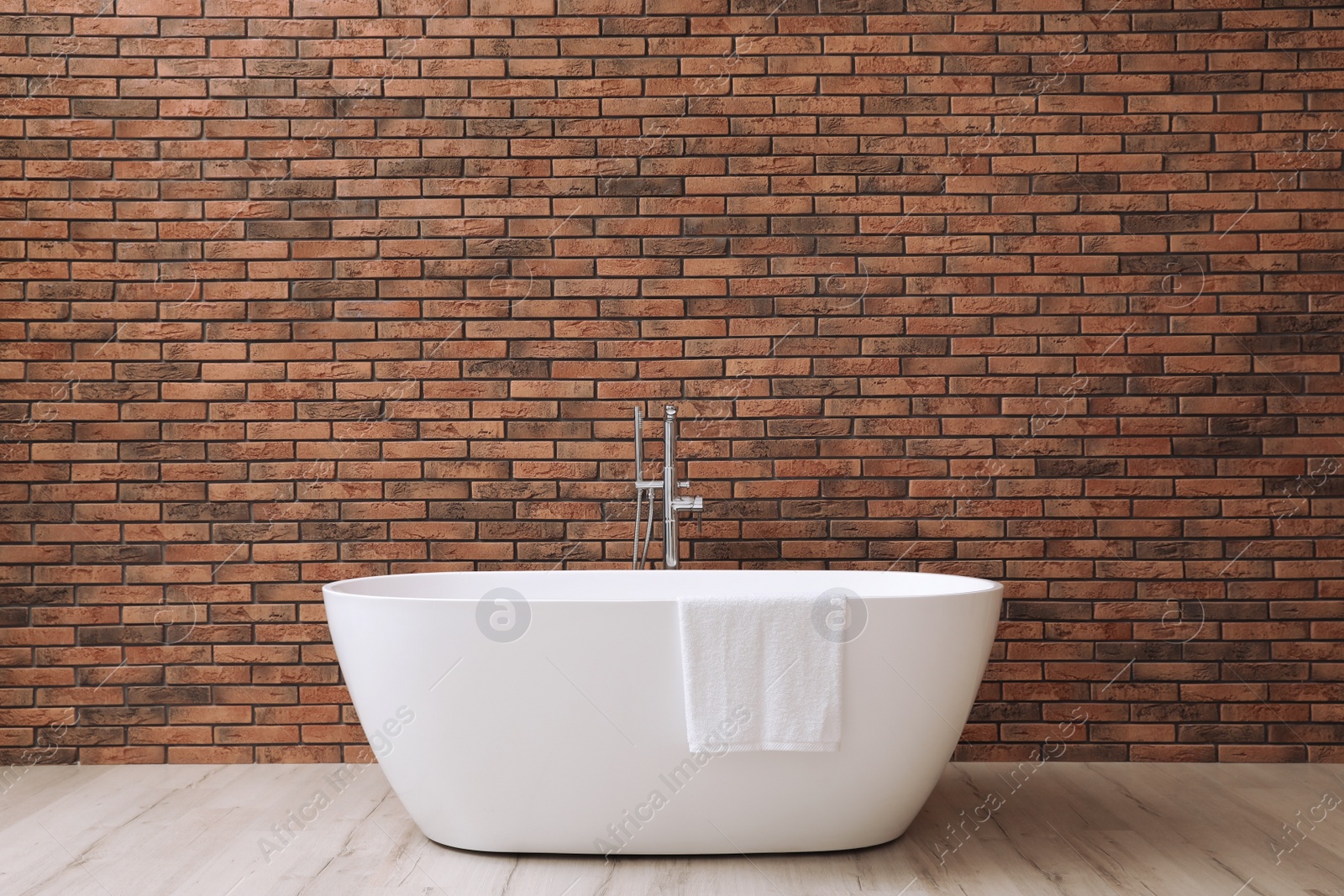 Photo of Modern ceramic bathtub with towel near brick wall