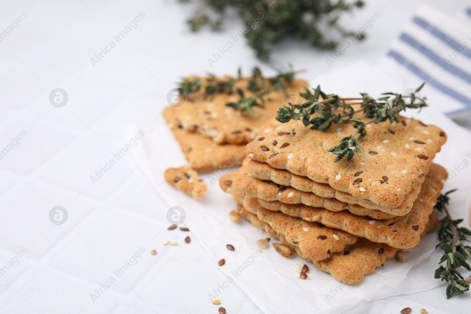 Photo of Cereal crackers with flax, sesame seeds and thyme on white tiled table, closeup. Space for text