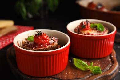 Photo of Baked eggplant with tomatoes, cheese and basil in ramekins on wooden board, closeup