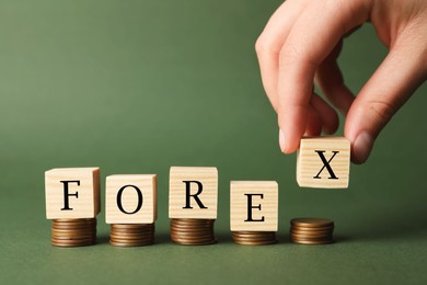 Photo of Woman putting cubes with word Forex on stacked coins against green background, closeup