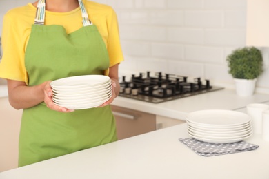 Photo of Woman holding stack of clean dishes in kitchen