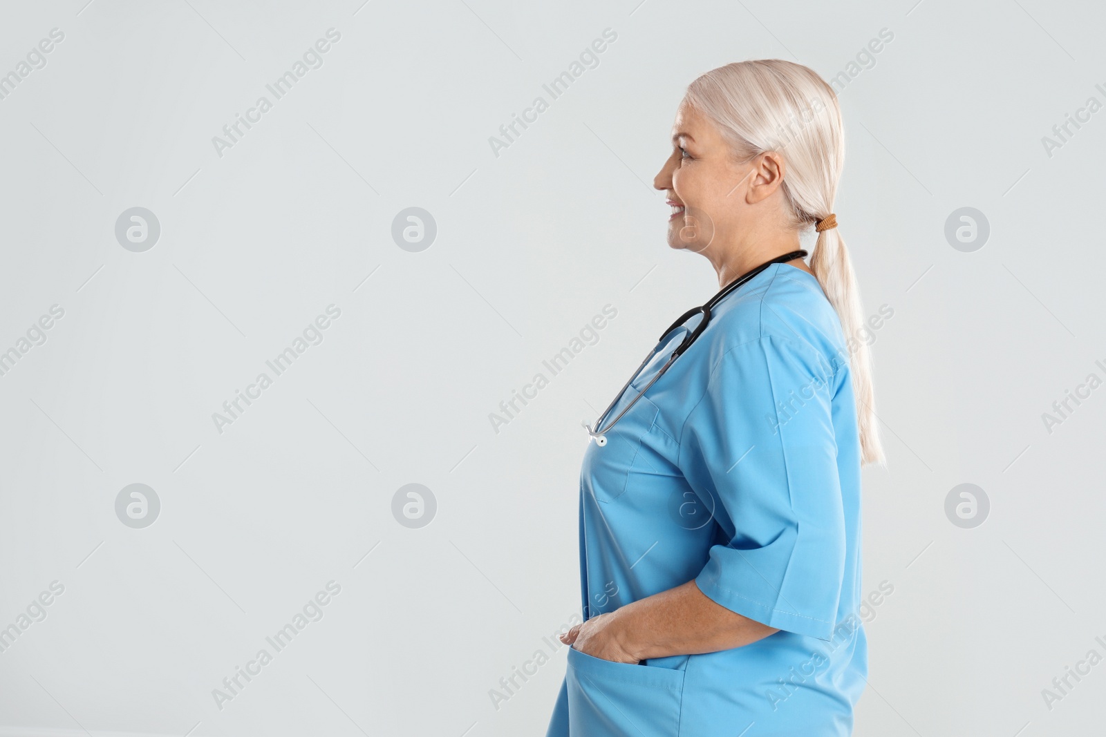 Photo of Mature doctor with stethoscope on light grey background. Space for text