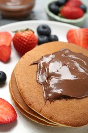 Tasty pancakes with chocolate paste and berries on plate, closeup