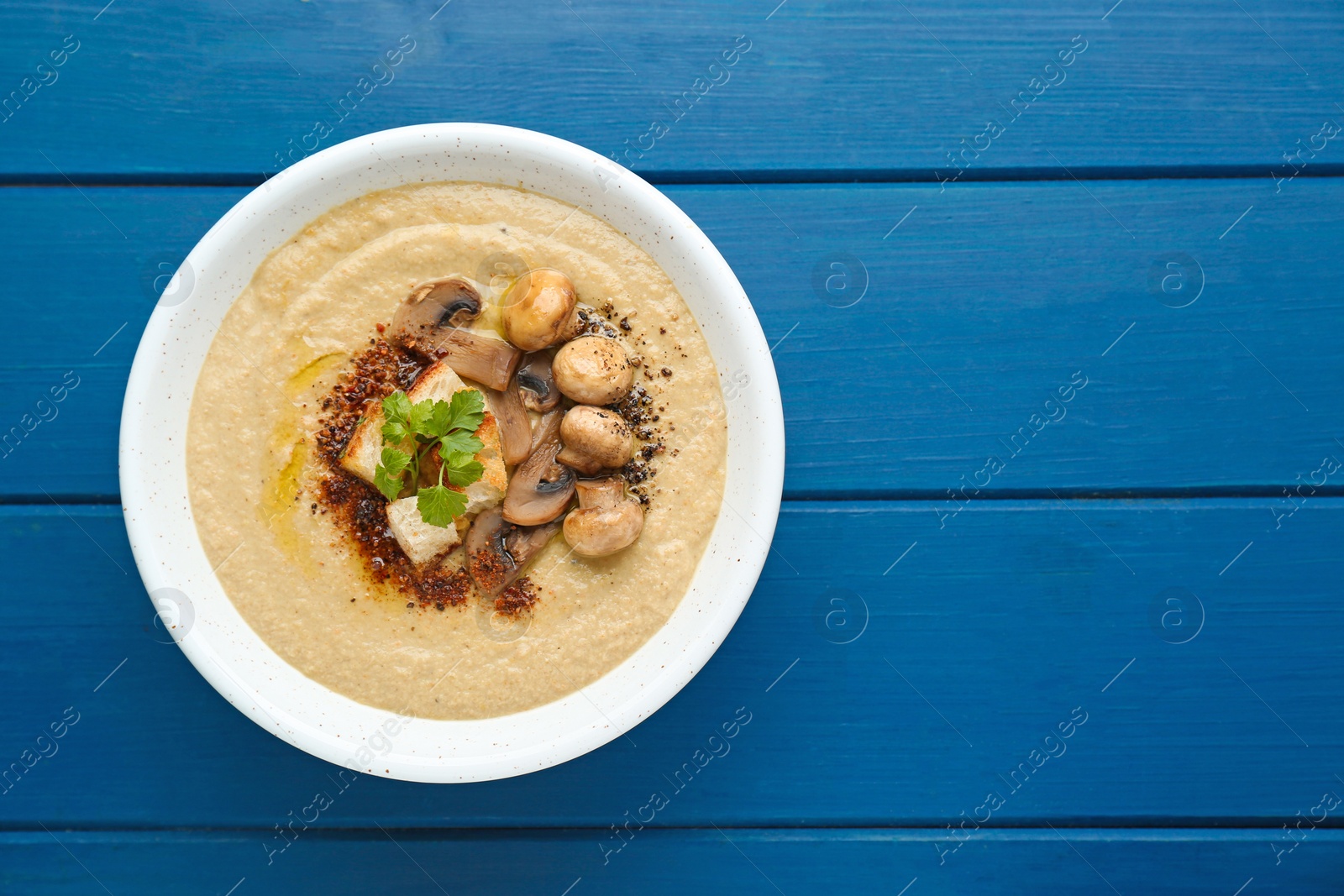 Photo of Delicious cream soup with mushrooms on blue wooden table, top view. Space for text