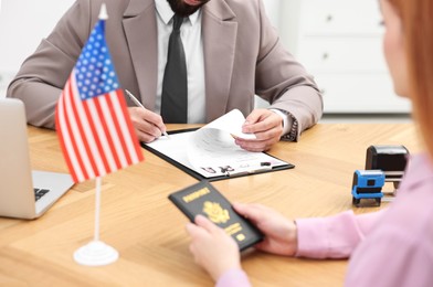 Photo of Immigration to United States of America. Embassy worker approving visa application form to woman in office, closeup