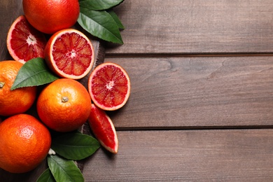 Photo of Ripe red oranges with green leaves on wooden table, top view. Space for text