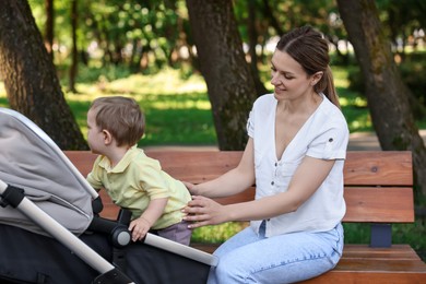 Happy nanny with cute little boy in stroller in park