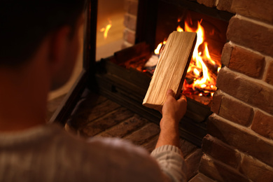 Photo of Man putting dry firewood into fireplace at home, closeup. Winter vacation