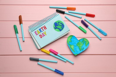 Photo of Happy Earth Day. Flat lay composition with notebook and markers on pink wooden table