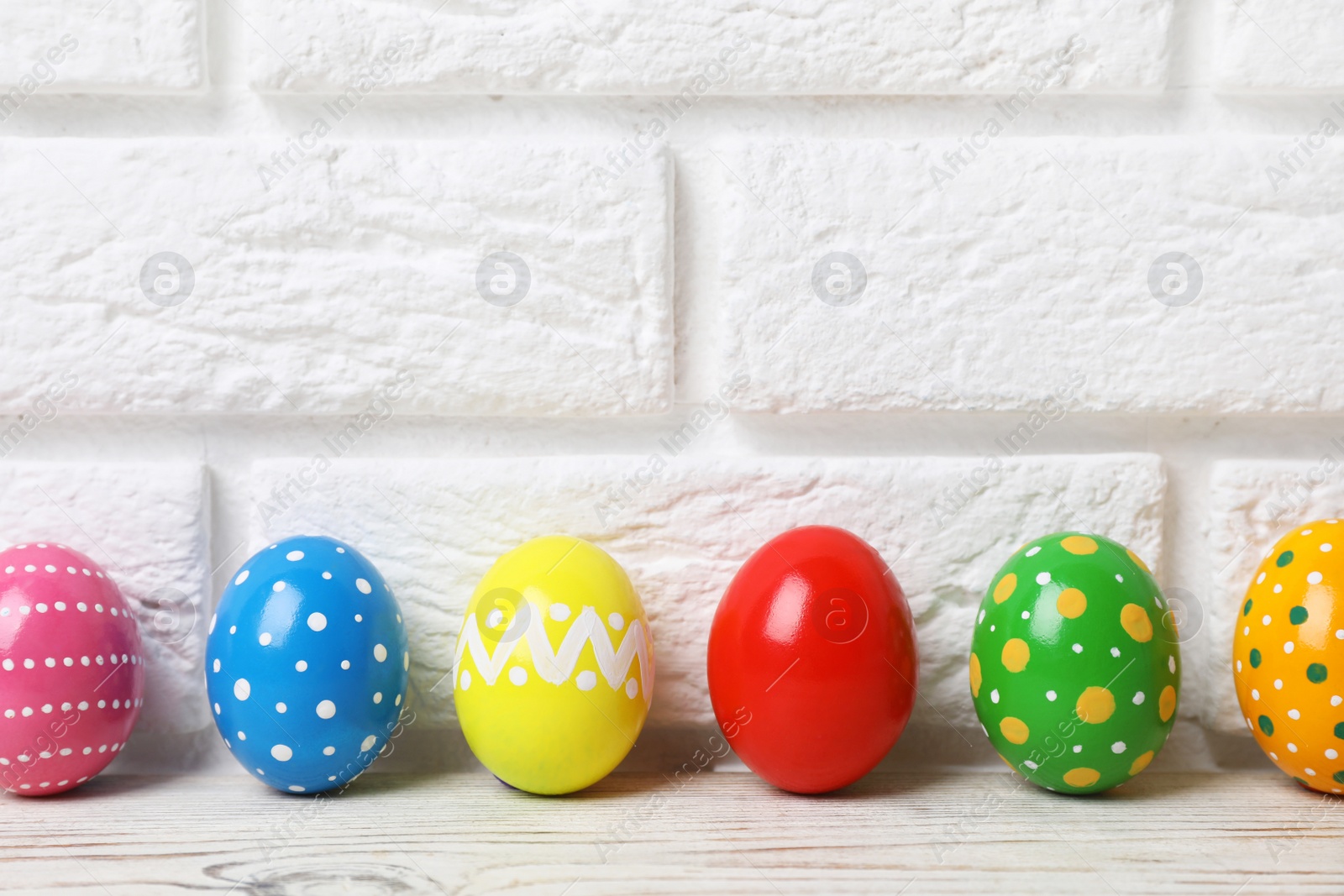 Photo of Decorated Easter eggs on table near brick wall. Space for text