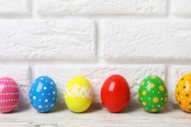 Decorated Easter eggs on table near brick wall. Space for text