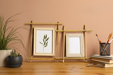 Photo of Stylish bamboo frames, potted houseplants and stationery on wooden table near brown wall