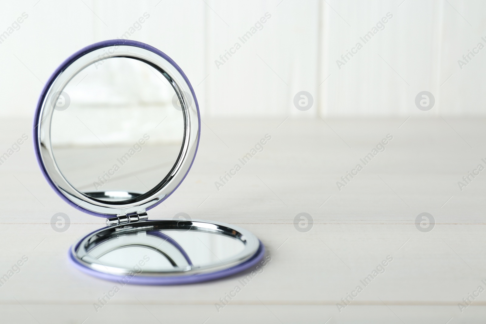Photo of Stylish cosmetic pocket mirror on white wooden table. Space for text