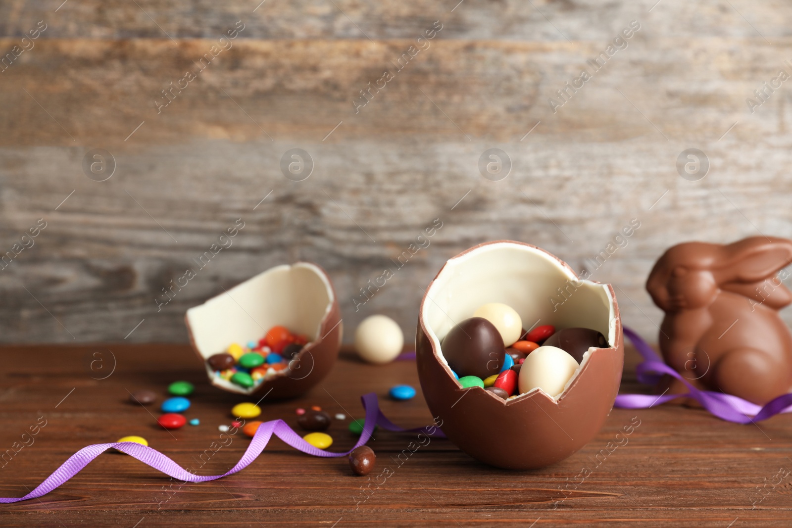 Photo of Broken chocolate Easter egg with candies on wooden table. Space for text