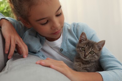 Photo of Cute little girl with kitten on sofa at home. Childhood pet