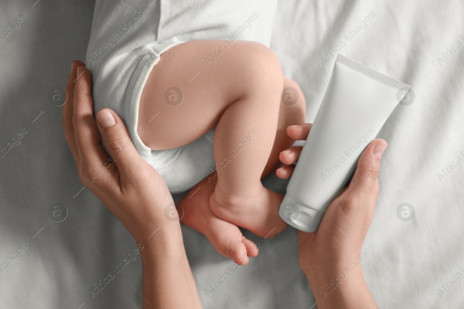 Photo of Mother with cream near little baby on bed, top view