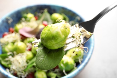 Photo of Fork with delicious Brussels sprouts salad over table, closeup