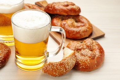 Photo of Tasty pretzels and glasses of beer on white wooden table