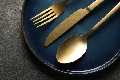 Stylish golden cutlery and plate on grey table, top view