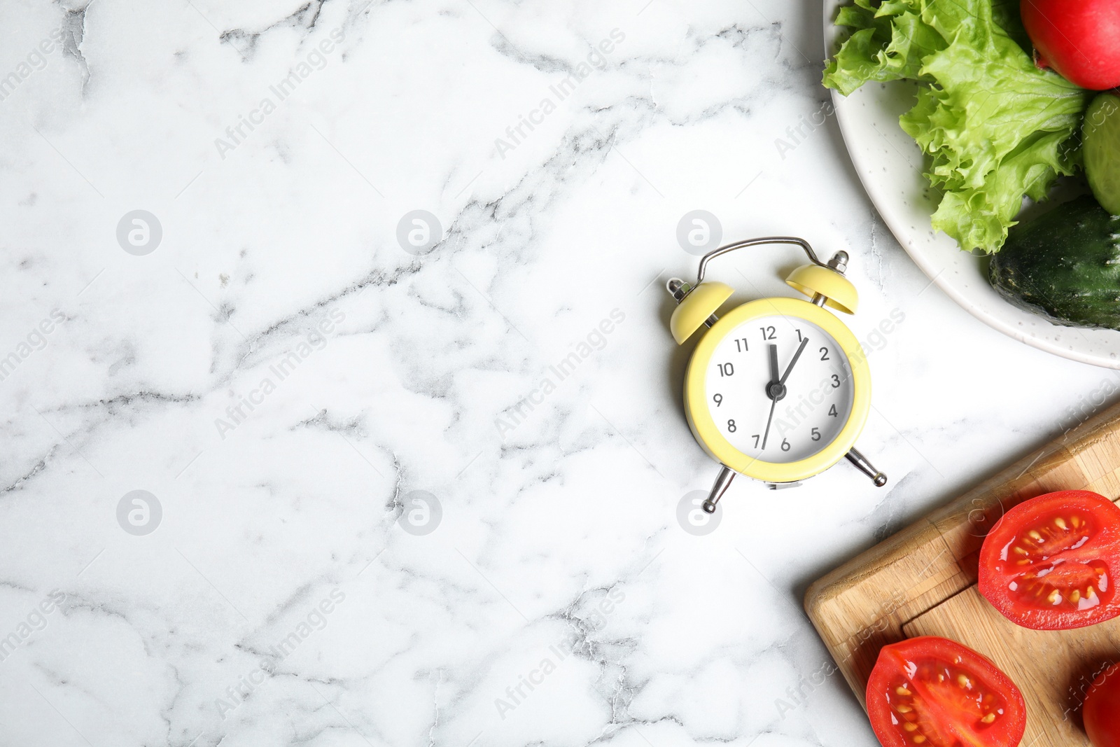 Photo of Alarm clock and vegetables on white marble table, flat lay with space for text. Meal timing concept