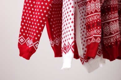 Different Christmas sweaters hanging on light background, closeup