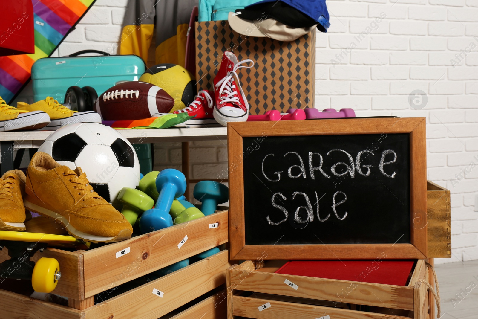 Photo of Sign Garage Sale written on blackboard near many different stuff indoors